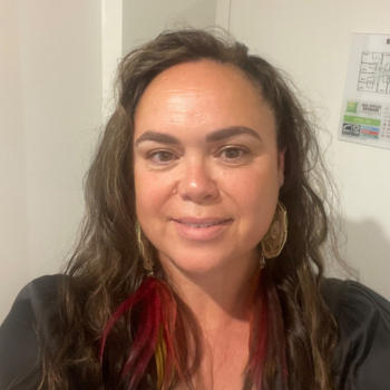 Woman with long wavy hair and earrings smiling indoors against light wall
